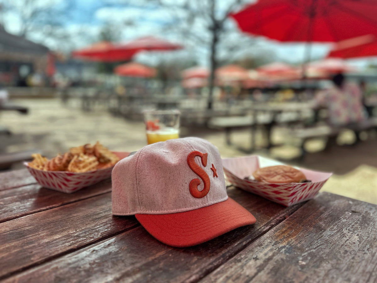 Southside Golf Co heritage golf hat in cream and burnt orange on outdoor table in Austin Texas