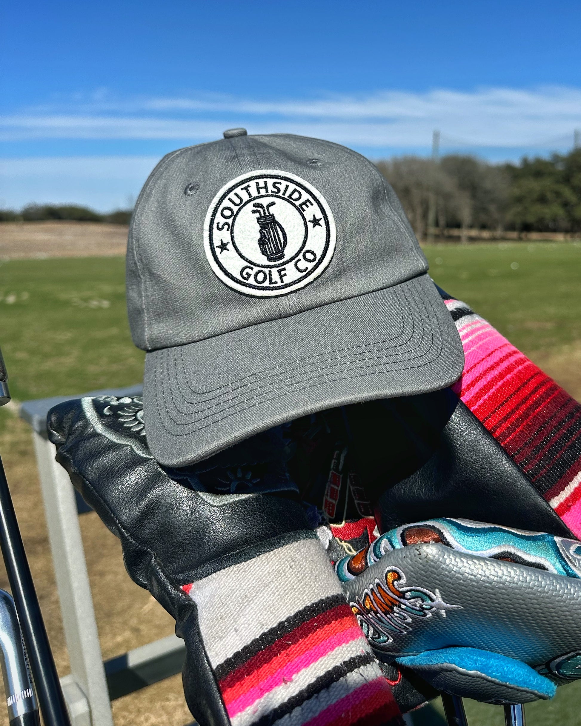 Southside Golf Co grey golf hat resting on golf bag with headcovers at driving range.