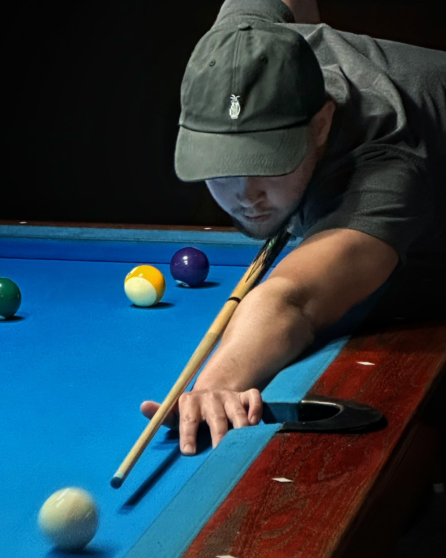 Golfer wearing a black Southside Golf Co. dad hat while lining up a pool shot on a blue billiards table.