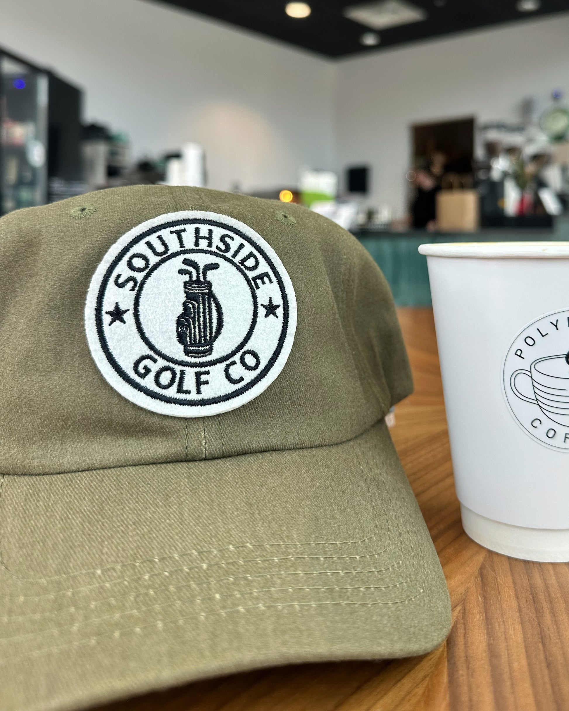 Green cap with Southside Golf Co logo next to a white cup with a coffee shop background