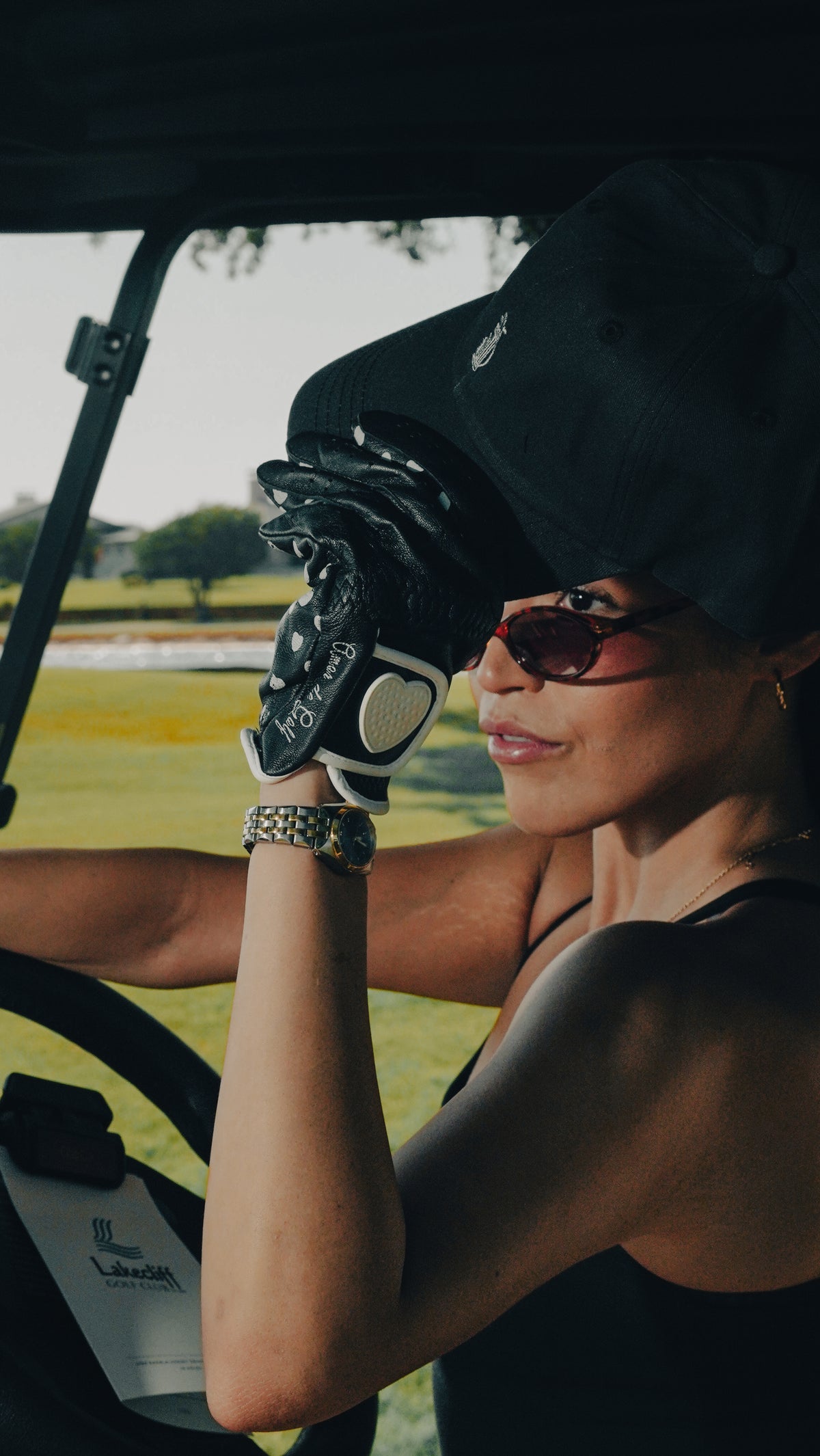 Woman wearing a black Southside Golf Co dad hat and golf glove while sitting in a golf cart.