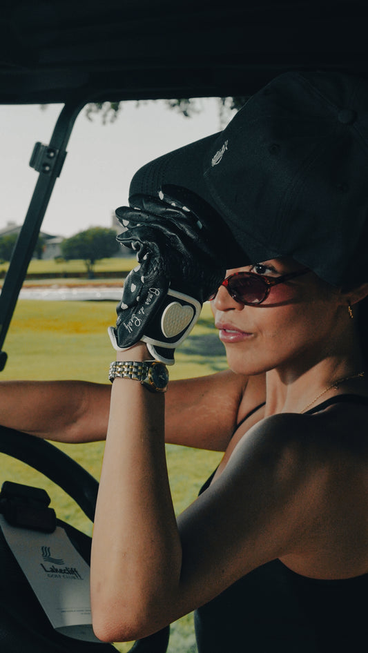 Woman wearing a black Southside Golf Co dad hat and golf glove while sitting in a golf cart.